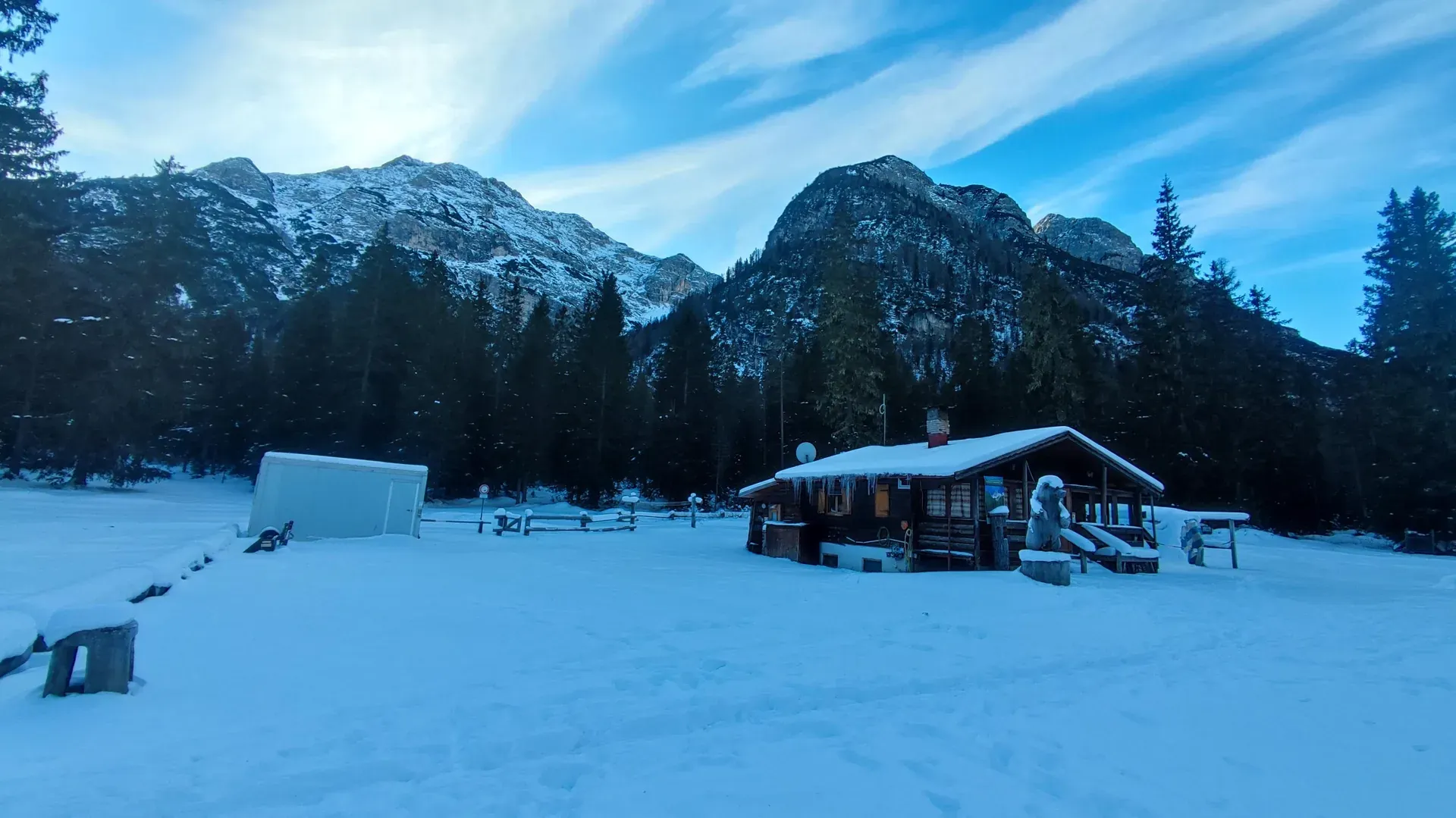 Baita alpina coberta de neve nas Dolomitas, com luz quente nas janelas e montanhas ao fundo — atmosfera típica de rifugio no inverno
