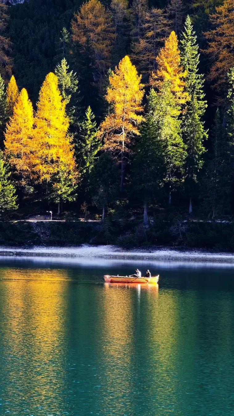 Casa de barcos e águas esmeralda do Lago di Braies no outono sob picos nevados