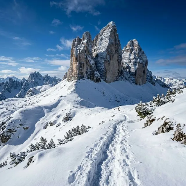 Vista de inverno das Tre Cime di Lavaredo com picos nevados e trilha marcada na neve fresca