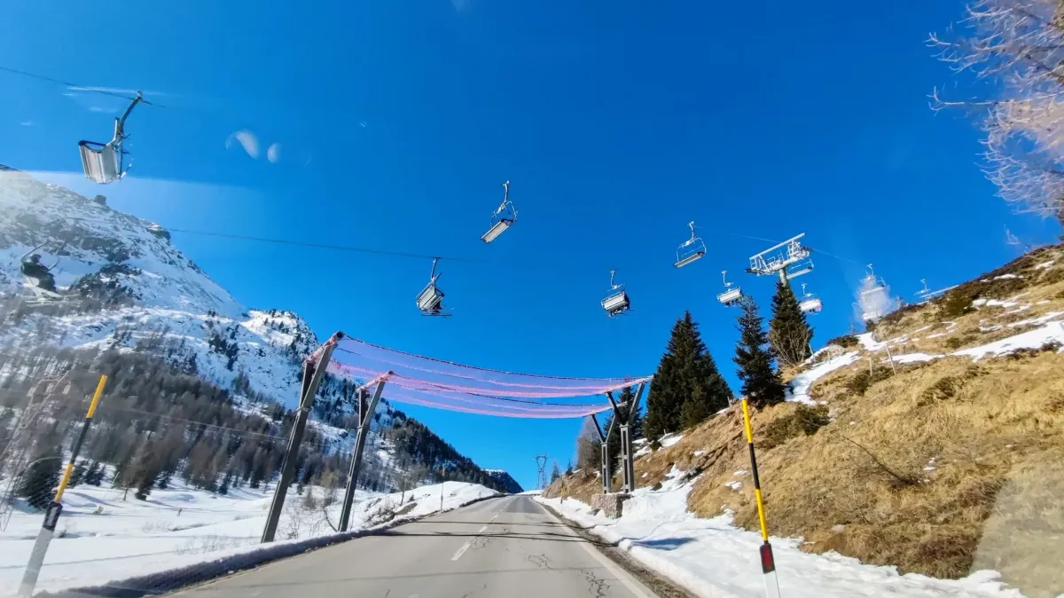 Esquiadores descendo pistas do Val di Fassa nas Dolomitas com picos nevados ao fundo em dia de sol.