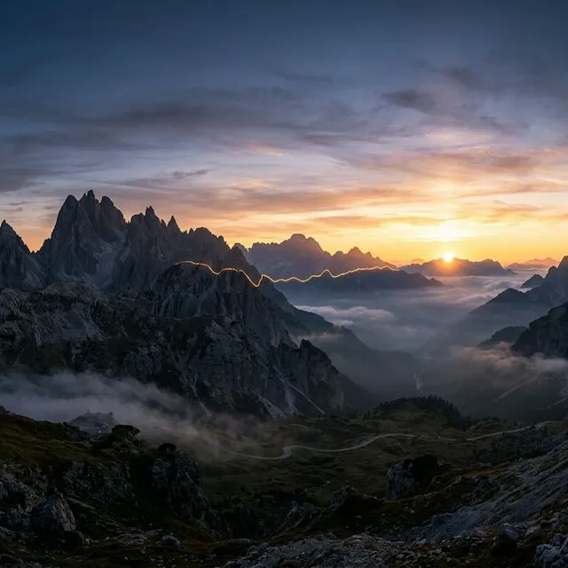 Nascer do sol no topo do Passo Giau com luz dourada sobre os picos rochosos e mar de nuvens no vale